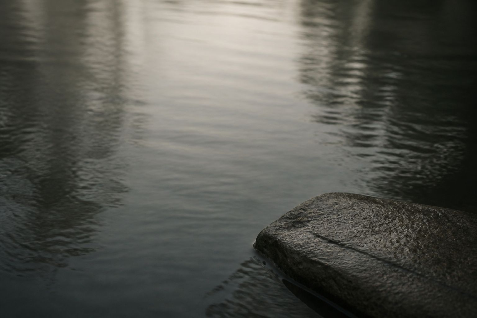The still surface of dark water beside a wet stone edge